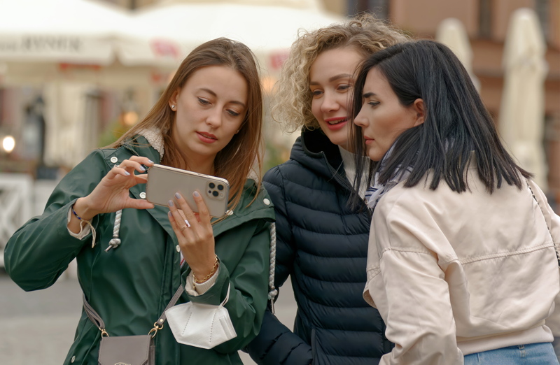 3 - Three women looking at a smartphone together outdoors in an urban setting
